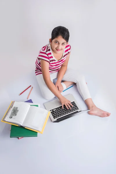 Cute little indian girl studying on laptop, asian small girl studying and using laptop, innocent indian girl child and study concept with pile of books & laptop