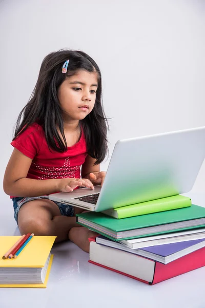Cute little indian girl studying on laptop, asian small girl studying and using laptop, innocent indian girl child and study concept with pile of books & laptop
