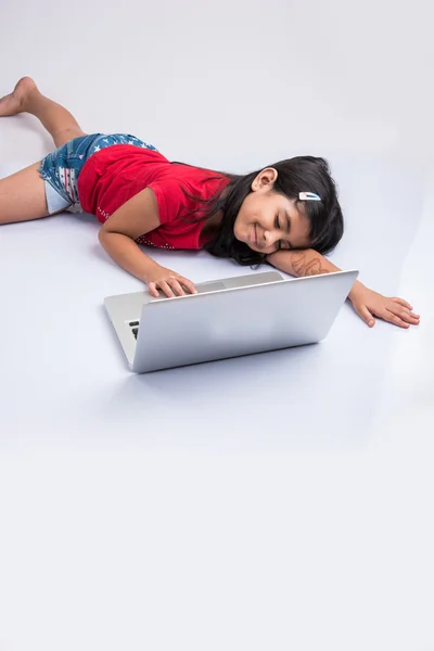 Indian little girl feeling sleepy using laptop, asian small girl playing on laptop, isolated over white background, cute indian baby girl lying on floor playing on laptop