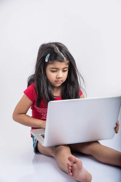 Cheerful indian little girl using laptop, asian small girl playing on laptop, isolated over white background, cute indian baby girl lying on floor playing on laptop