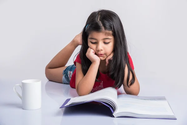 Indian small girl reading book, asian girl child reading book over white background, cute 5 year old indian small girl reading book with milk mug