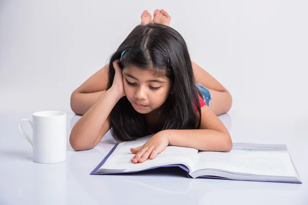 Indian small girl reading book, asian girl child reading book over white background, cute 5 year old indian small girl reading book with milk mug