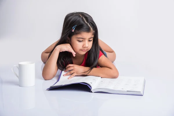 Indian small girl reading book, asian girl child reading book over white background, cute 5 year old indian small girl reading book with milk mug