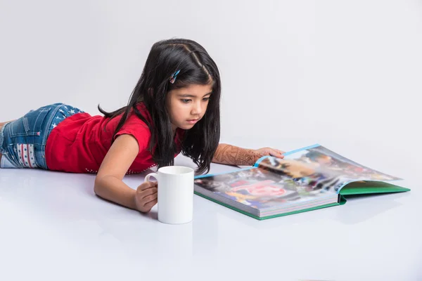 Indian small girl reading book, asian girl child reading book over white background, cute 5 year old indian small girl reading book with milk mug