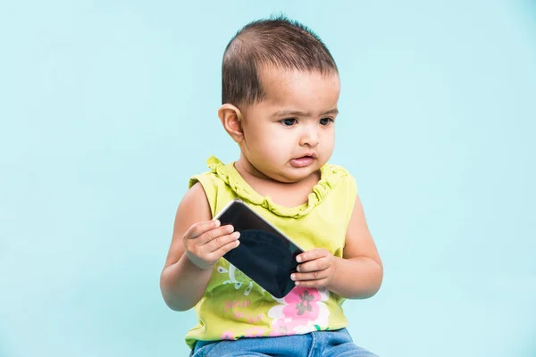 Happy baby girl talking on mobile phone isolated on blue. Closeup. Indian little girl and mobile or handset, asian baby girl using smartphone
