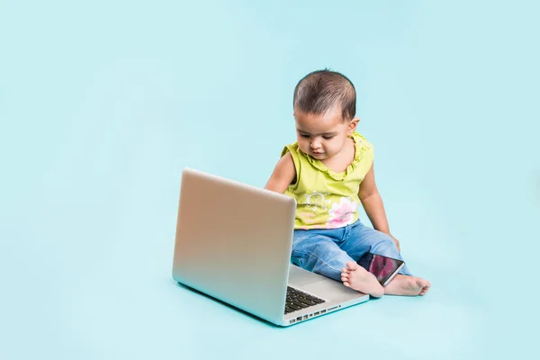 Baby sitting on the floor with a laptop, indian baby girl with laptop over blue background, indian baby girl playing with laptop, asian baby girl with laptop