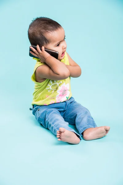 Happy baby girl talking on mobile phone isolated on blue. Closeup. Indian little girl and mobile or handset, asian baby girl using smartphone