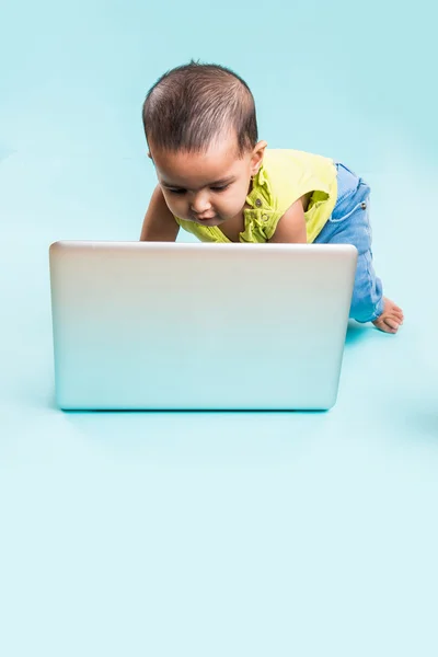Baby sitting on the floor with a laptop, indian baby girl with laptop over blue background, indian baby girl playing with laptop, asian baby girl with laptop