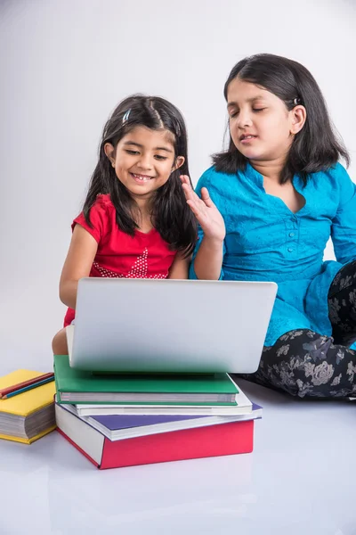 Two indian small girls studying on laptop with pile of books, asian small girls and homework using laptop, group study concept