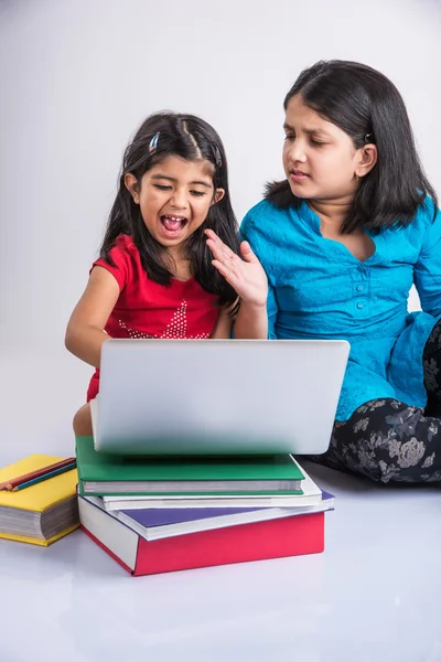 Two indian small girls studying on laptop with pile of books, asian small girls and homework using laptop, group study concept