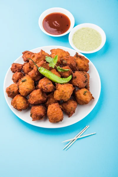 Delicious Tasty and Yummy Indian Moong Dal vada or moong dal pakoda or moong vade or Pakora (Fritter) with fried green chilli, red and green hot sauce.