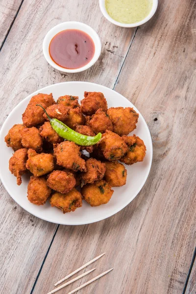 Delicious Tasty and Yummy Indian Moong Dal vada or moong dal pakoda or moong vade or Pakora (Fritter) with fried green chilli, red and green hot sauce.