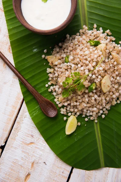 Sabudana Khichadi - An authentic dish from Maharashtra made with sago seeds served over coconut leaf with curd in a wooden bowl