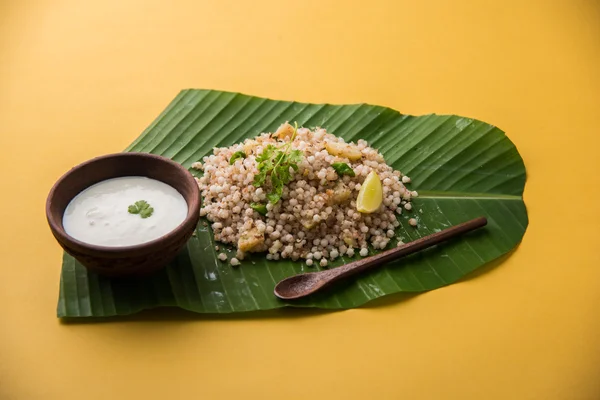 Sabudana Khichadi - An authentic dish from Maharashtra made with sago seeds served over coconut leaf with curd in a wooden bowl