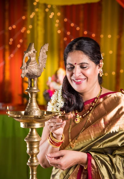 Indian woman in traditional saree lighting oil lamp or samai with diya and celebrating ganesh festival or Diwali or deepavali. Indian lady holding oil lamp indoors.