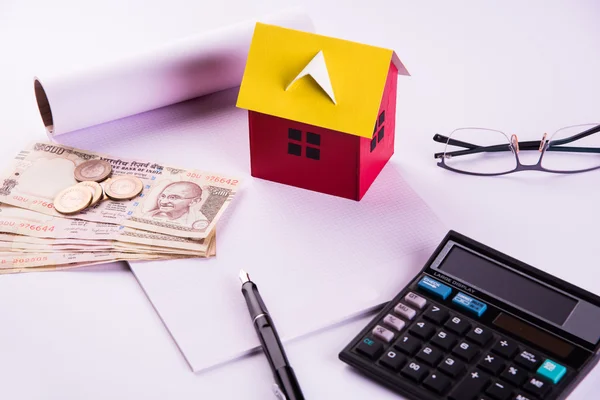 Buying home on loan or rent concept using model house, calculator, indian currency notes, pen and spectacles