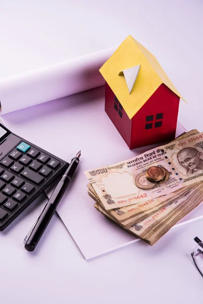 Buying home on loan or rent concept using model house, calculator, indian currency notes, pen and spectacles