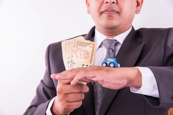 Indian businessman holding currency notes and toy car with key, buying car concept