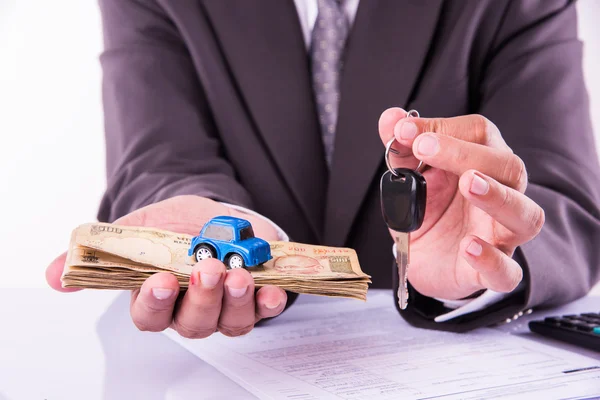 Indian businessman holding currency notes and toy car with key, buying car concept