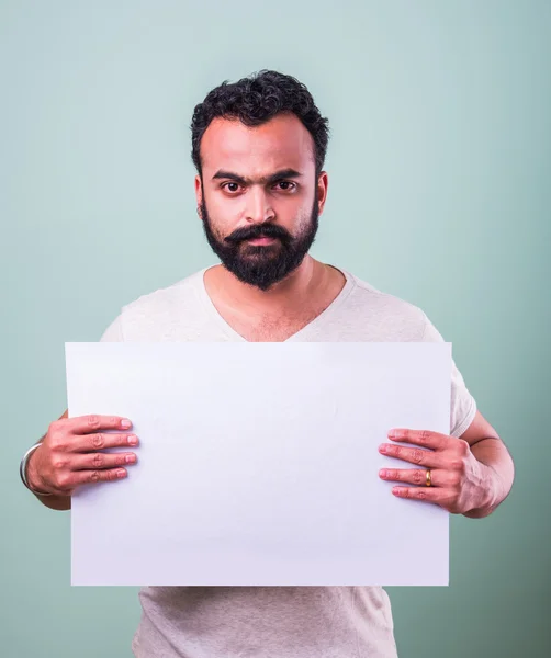 Portrait of handsome indian man with beard holding white blank board. Indian Man holding blank poster.