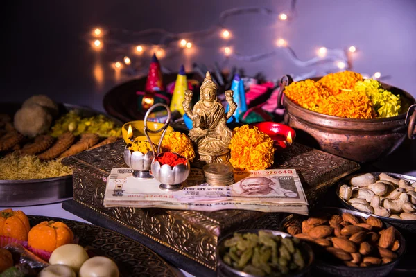 Oil lamp or diya with crackers, sweet or mithai, dry fruits, indian currency notes, marigold flower and statue of Goddess Laxmi or lakshmi on diwali night