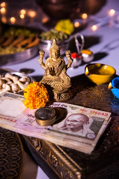 Oil lamp or diya with crackers, sweet or mithai, dry fruits, indian currency notes, marigold flower and statue of Goddess Laxmi or lakshmi on diwali night