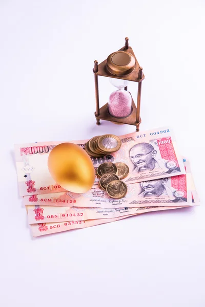 Hourglass with Golden egg and indian money or indian currency over white background. Shallow focus.