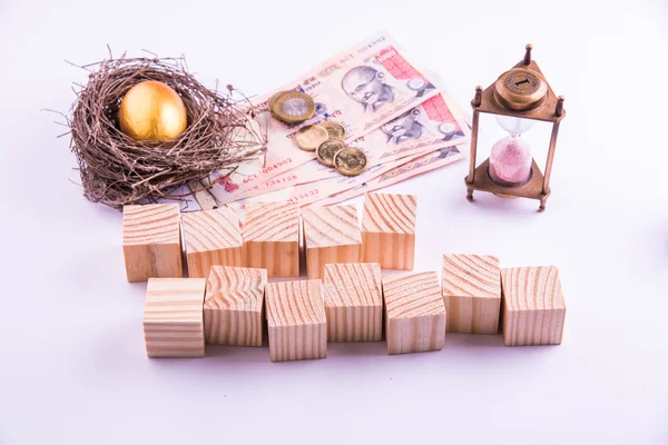 Indian currency notes with coins and golden egg along with antique sand clock and wooden blocks with FIXED DEPOSIT alphabates written over it