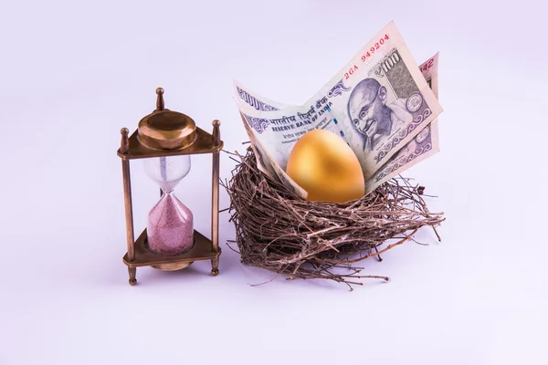 Hourglass with Golden egg and indian money or indian currency note in a real nest. Shallow focus.