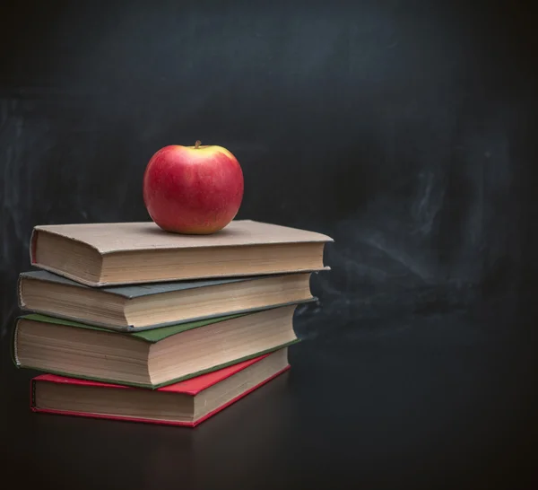 Stack of books and juicy apple on a background of black school board