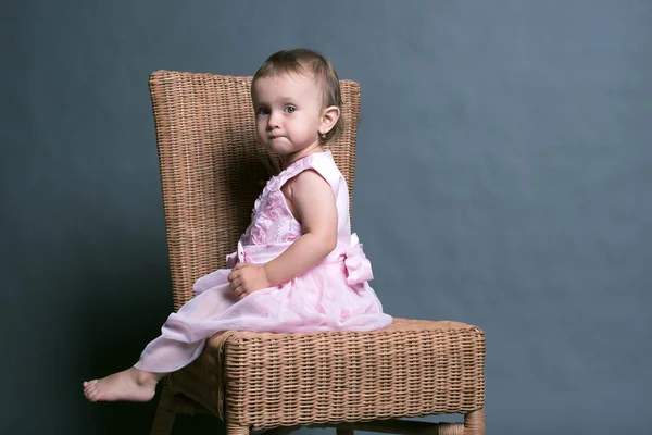 Little girl in a pink dress sits on a chair