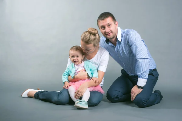 Father, mother and daughter sitting on a gray background and build a toy house
