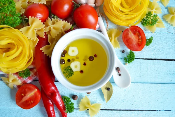 Blue food background with olive oil, raw pasta and tomato