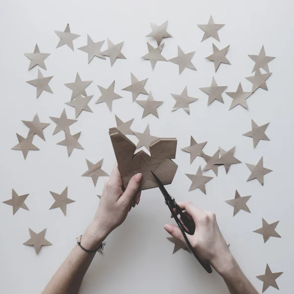 Woman's hands on the table cut stars of craft paper by Japanese scissors. New Year, Christmas preparation.