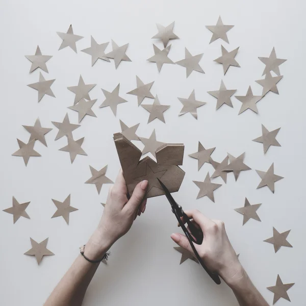 Woman\'s hands on the table cut stars of craft paper by Japanese scissors. New Year, Christmas preparation.