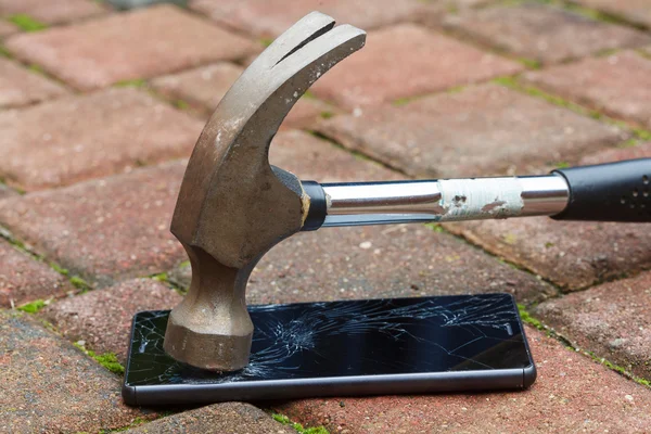 Broken mobile phone hit by hammer lying on pavement
