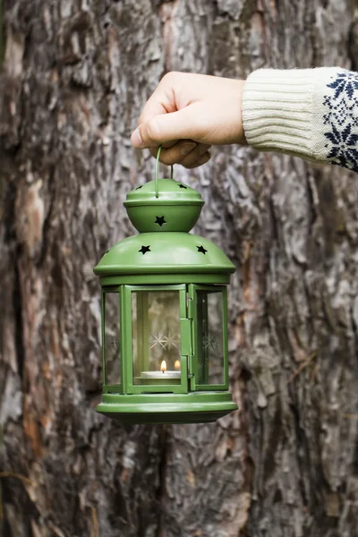 Hand holds green lantern on wooden background