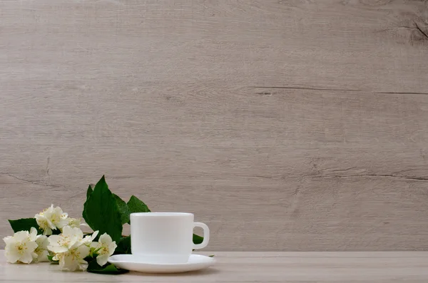 White mug and a branch of jasmine on the wood background, space for text
