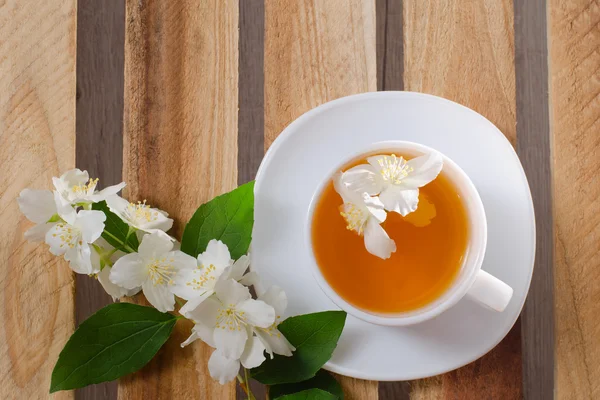 Top view of a cup of tea with a sprig of jasmine flowers and a wooden table