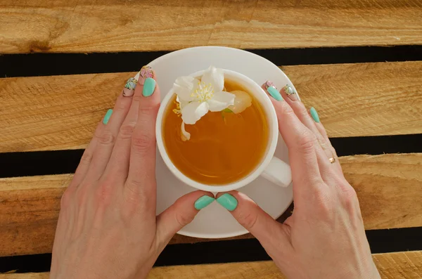 Female hand holding a mug of tea and jasmine flower, top view on a background of wooden planks