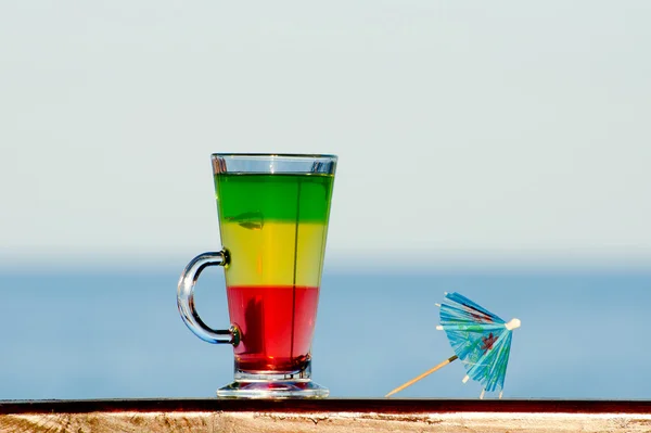 A glass with colorful cocktail on the background of the sea, umbrella for cocktails