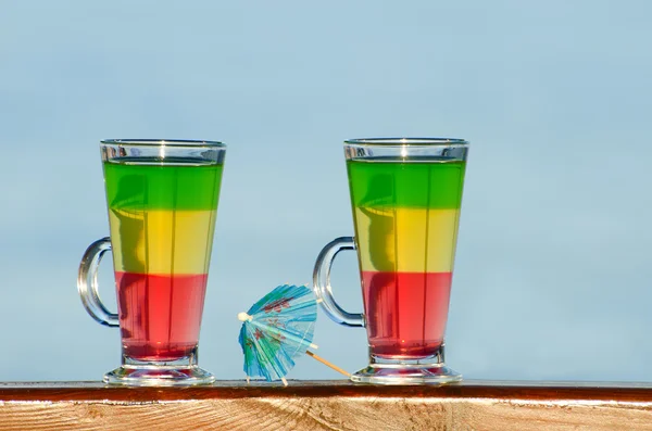 Two glasses with colorful cocktails on the background of the sea, umbrella for cocktails