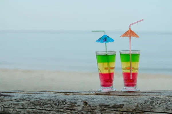 Two cocktails with straws on a log in the evening on the sea background, place for text