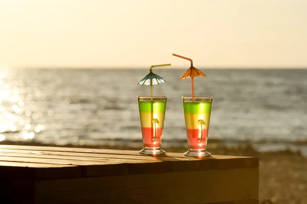 Two colorful cocktails in the morning sun on a wooden table on the beach against the sea