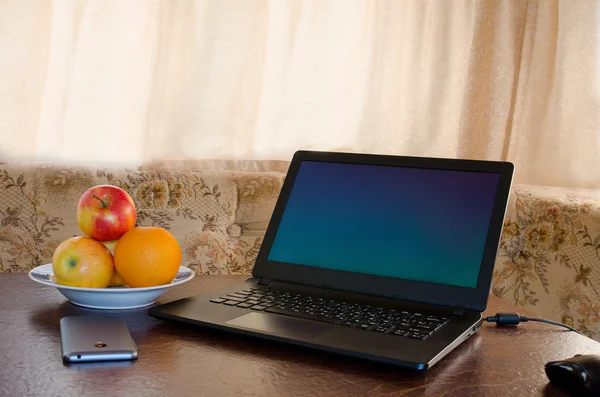 Laptop on a table in a cozy kitchen with a plate of fruit, a smartphone. Break