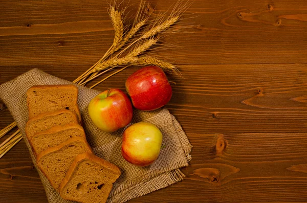 Sliced rye bread, apples and ears of corn on sackcloth, wooden table, top view
