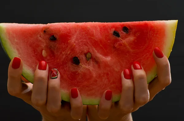 Large slice of ripe watermelon in female hands on a black background, close-up