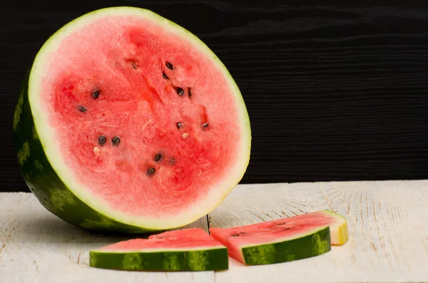 Halves cut watermelon slices on a light wooden table, black background