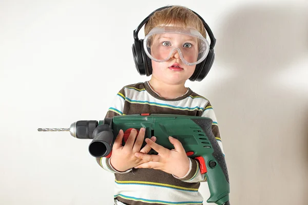 Surpised Little boy with protective glasses and headphones holding drill