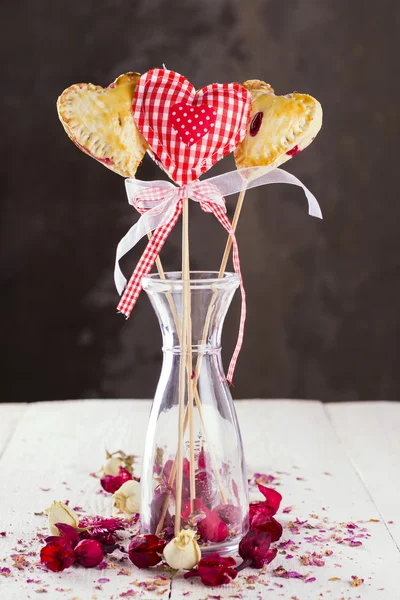 Cookies pops in the form of heart and heart from fabric in a pattern a red cage with buds of roses